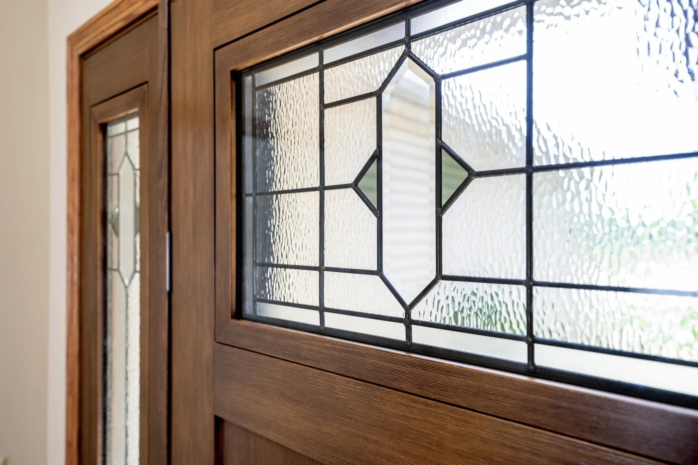 Rich and refined, this ProVia front entry door showcases intricate glasswork framed in warm, woodgrain detail. The patterned glass blends textured and clear elements for depth and light play, while a deep chestnut finish lends timeless character. Delicate metal caming weaves through the design, adding a touch of elegance without overwhelming the door’s classic charm.
