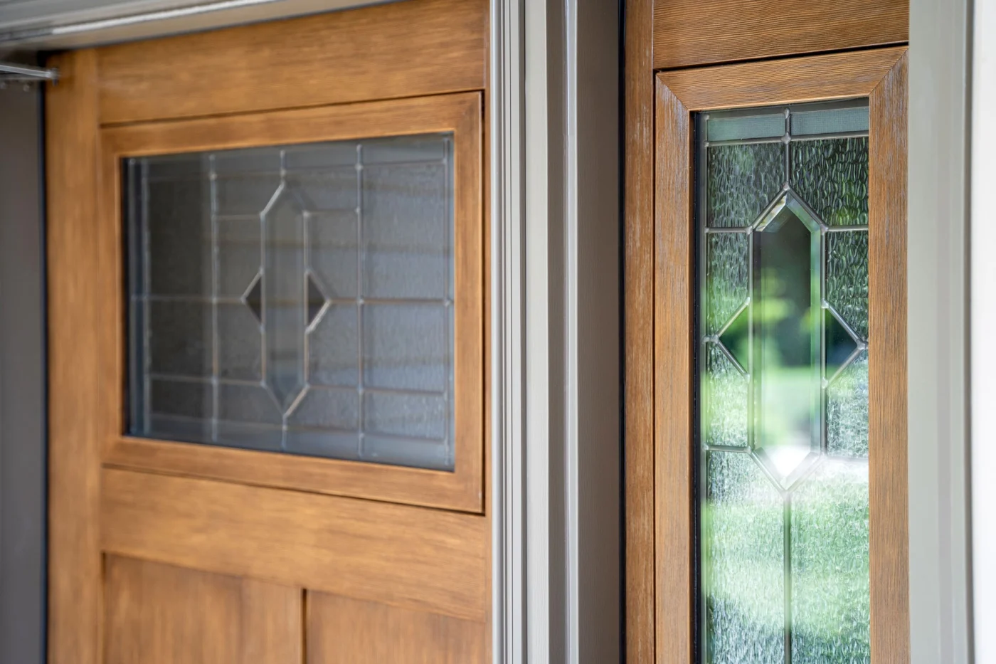 Close-up view of a ProVia Brookhaven decorative glass entry door and matching sidelite, framed in a warm woodgrain finish. The beveled and textured glass features an elegant diamond motif, creating a refined, light-catching focal point.