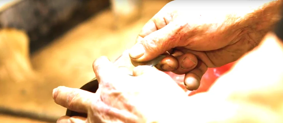 Close-up of skilled hands working with a decorative glass component in a manufacturing setting, showcasing the craftsmanship and precision behind ProVia’s front door designs.