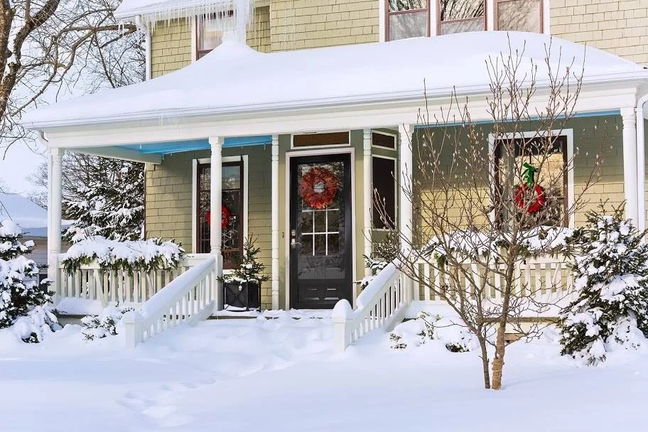 Snow-covered front porch of a home featuring a black ProVia front door with decorative glass panels and a festive wreath, demonstrating the door’s durability and style in harsh winter conditions.