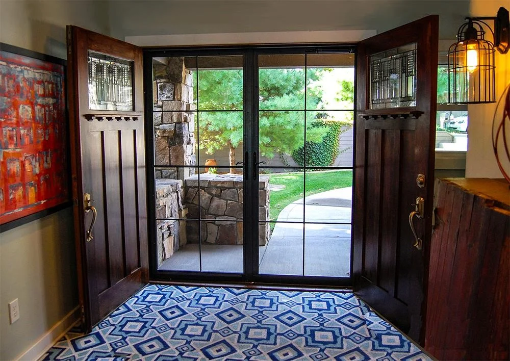 A custom double Home Guard security door with full-view glass panels and black grid muntins, framed by rich wood entry doors featuring decorative glass inserts.