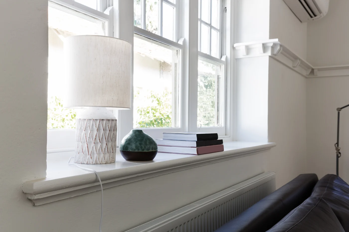 How To Replace Window Sash NY Metro | Quick Tutorial | Window King A bright, modern living room with tall white double-hung windows letting in natural light. A white ceramic lamp, small decorative vase, and stacked books sit neatly on the wide windowsill, creating a cozy and inviting space.