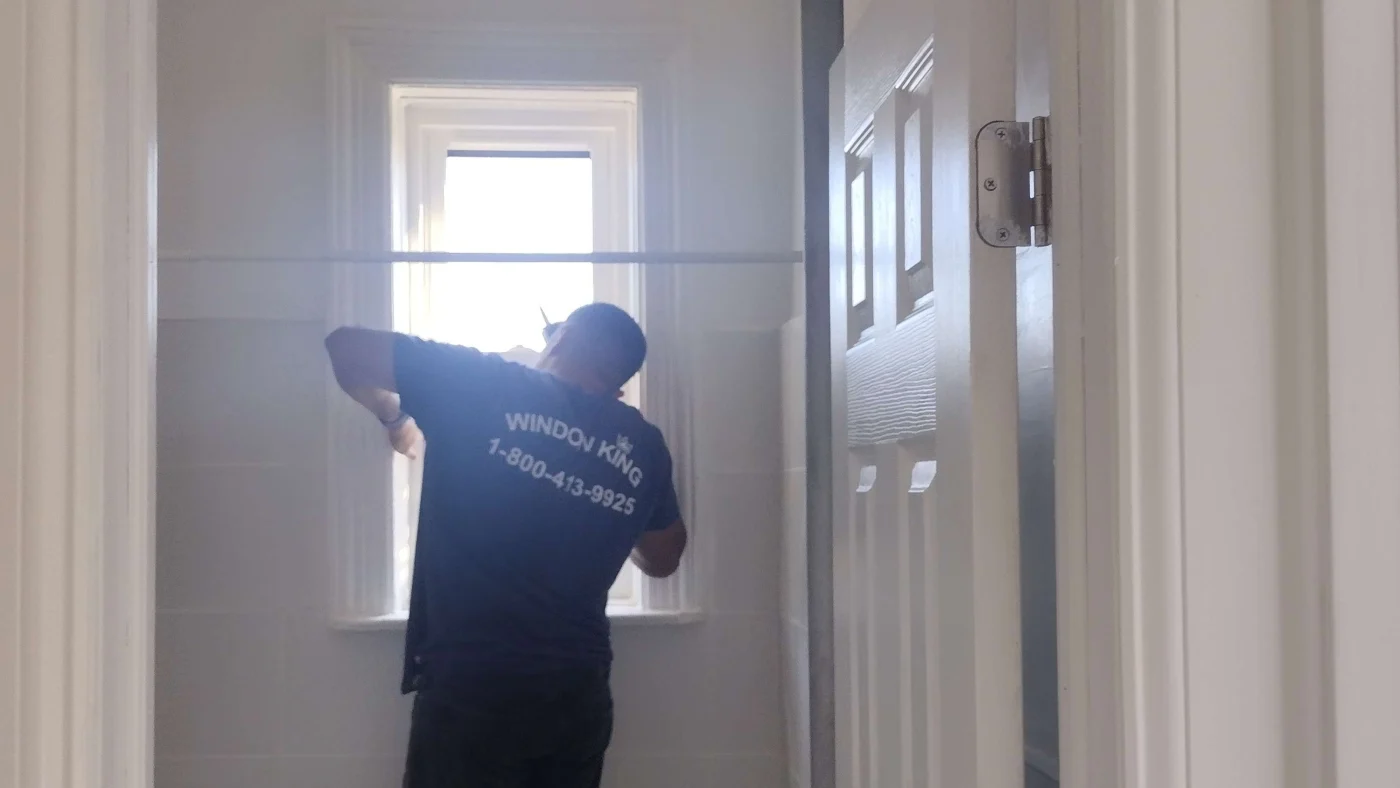 Skilled installer in a Window King shirt taking precise measurements on a window inside a home, highlighting training and thousands of completed projects.