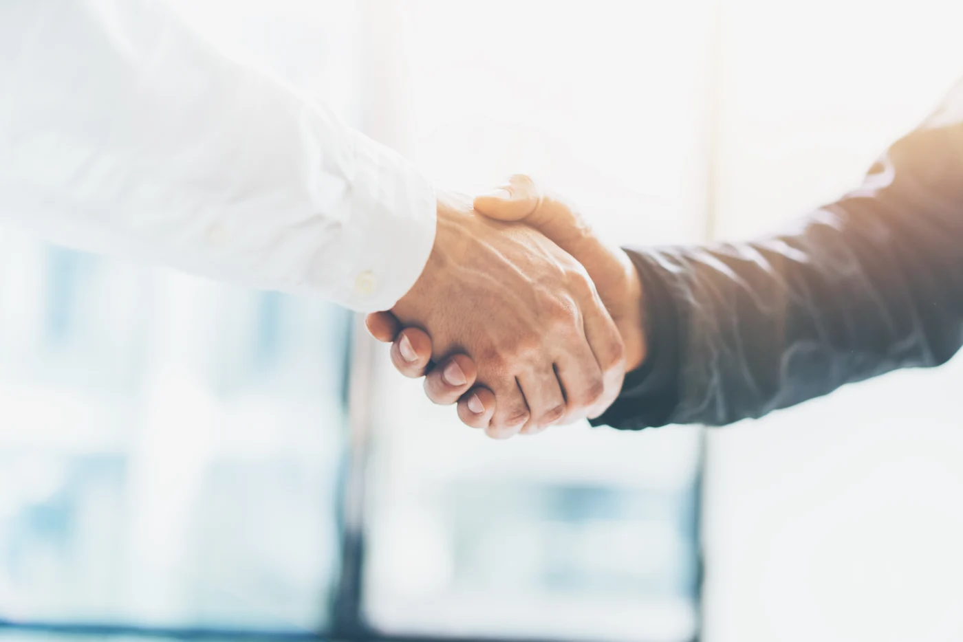 Two people shaking hands in natural light, representing the final walkthrough, elite workmanship, and a satisfied homeowner at project completion.