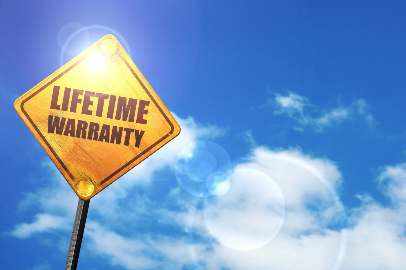 A yellow road-style sign reading “LIFETIME WARRANTY” stands against a bright blue sky with scattered clouds and sun flare.