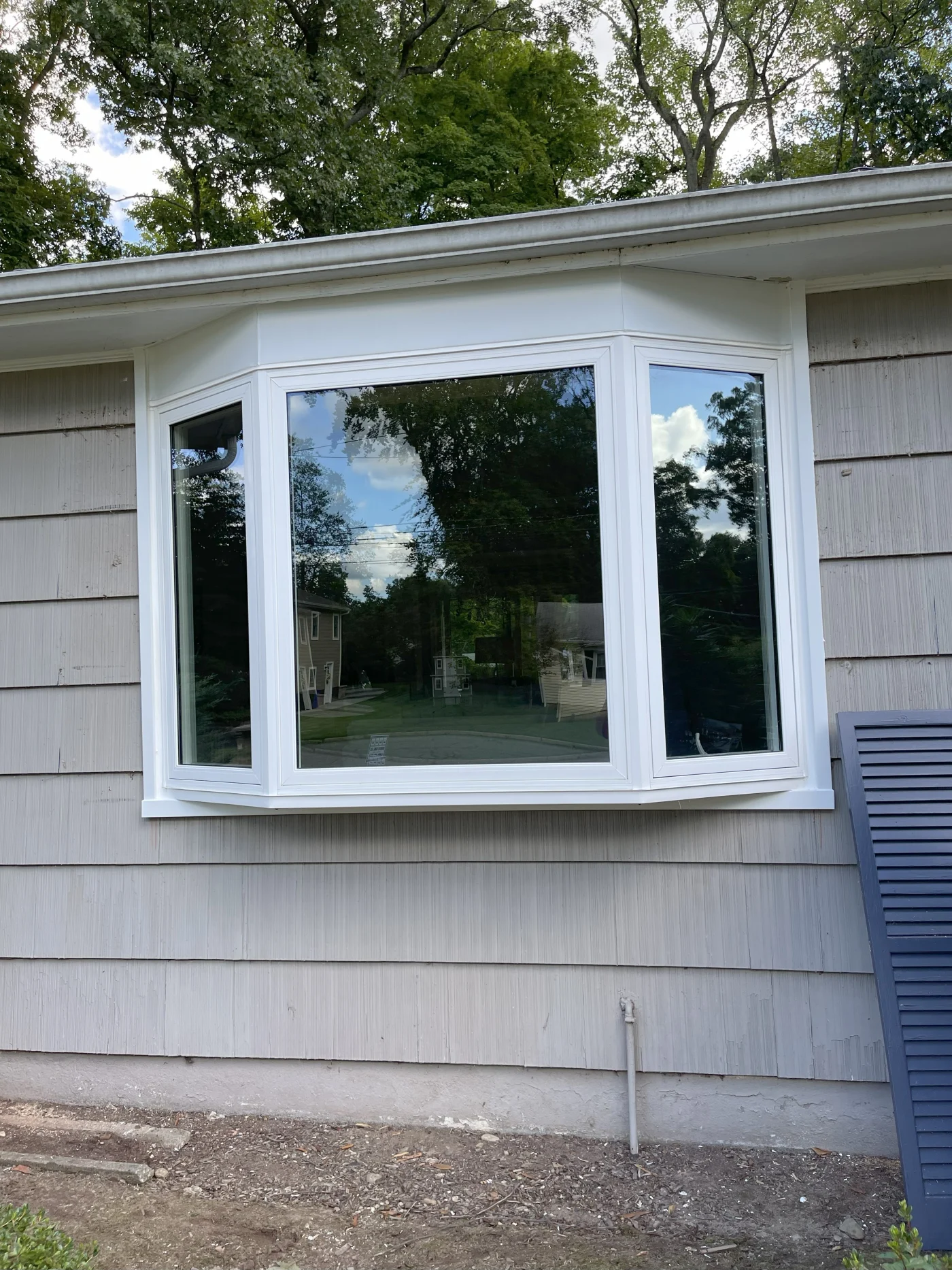 A bay window with three black-framed glass panels extends outward from the white siding of a house.