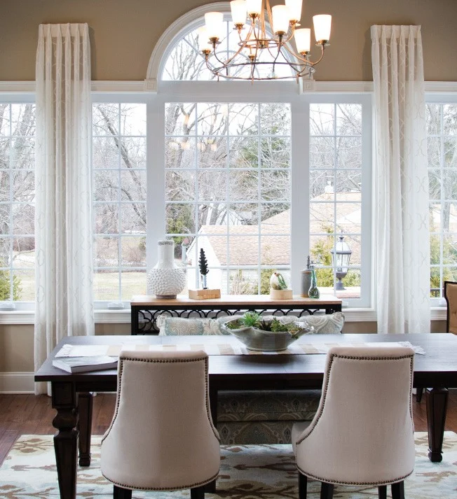 A beautifully lit dining room featuring expansive OKNA Casement 700 Series windows with elegant grille patterns and an arched transom. Framed in crisp white trim, the windows invite abundant natural light while maintaining excellent energy efficiency. Designed for smooth operation and timeless charm, these casements elevate both form and function – perfect for NY Metro homeowners who want more than just a view.