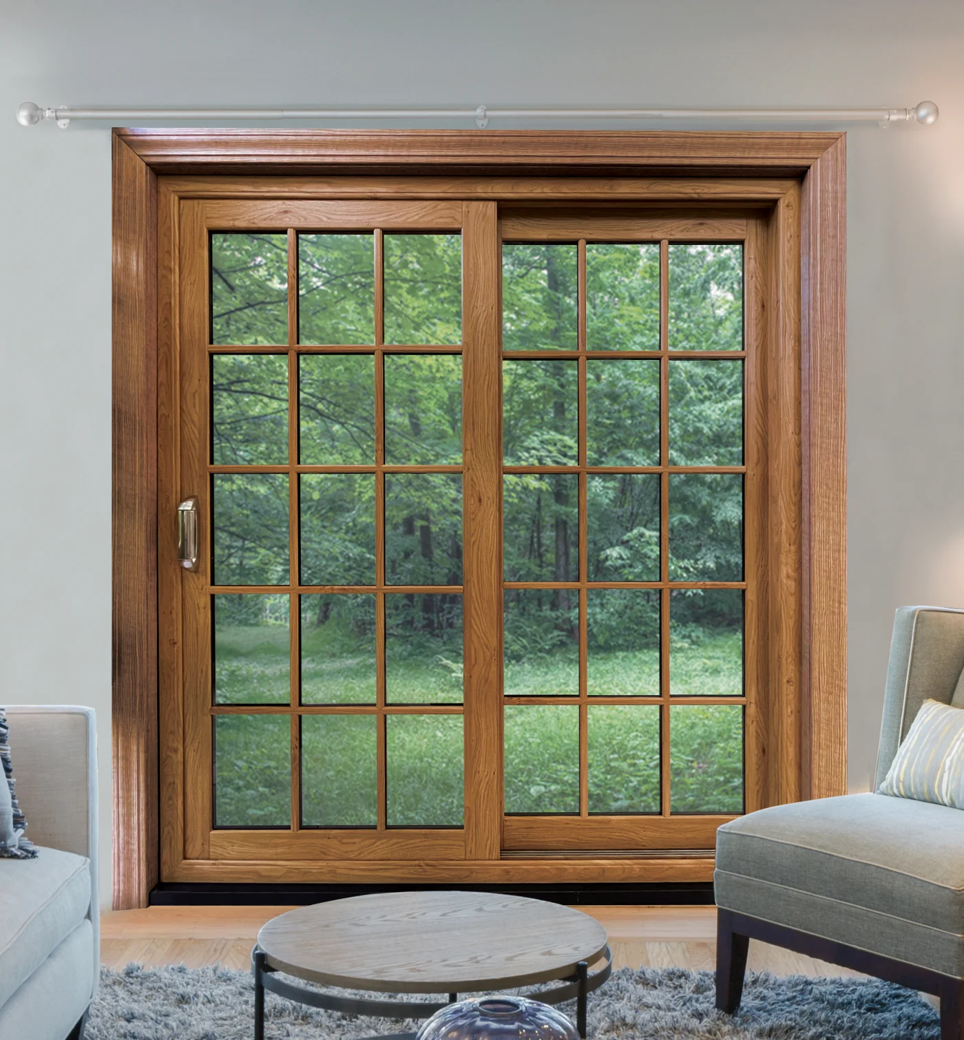 A warm and inviting living room featuring an OKNA Forester sliding patio door with a rich wood-grain finish. The door’s divided-light grid design gives it a timeless, traditional look, while expansive glass panels open the view to a lush, green backyard. Framed by matching wood trim, the Forester blends classic craftsmanship with durability, complementing the cozy interior décor of soft-toned furniture, a round coffee table, and a plush area rug.