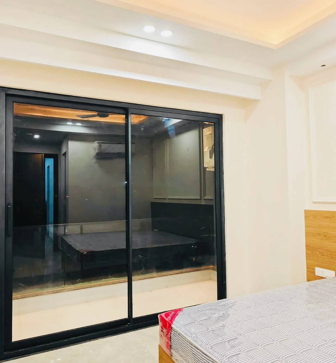 A wide OKNA sliding glass patio door in a modern bedroom, framed in sleek black and opening to an enclosed adjoining space.