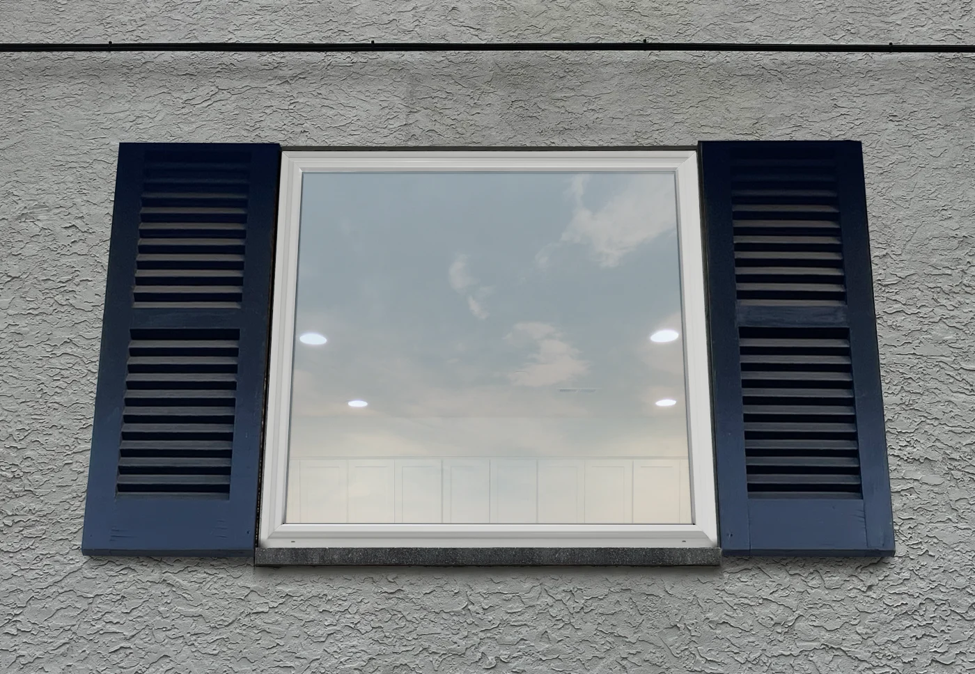 OKNA Window Installation Services – NY Metro, Tri-State – Window King An OKNA 400 series picture window installed on a home. The sleek, white frame and large, uninterrupted glass pane offer a clear view and reflect the sky beautifully, emphasizing the window’s energy-efficient design and modern aesthetic. Framed by deep blue shutters and set in textured stucco siding, the window blends curb appeal with top-tier performance.