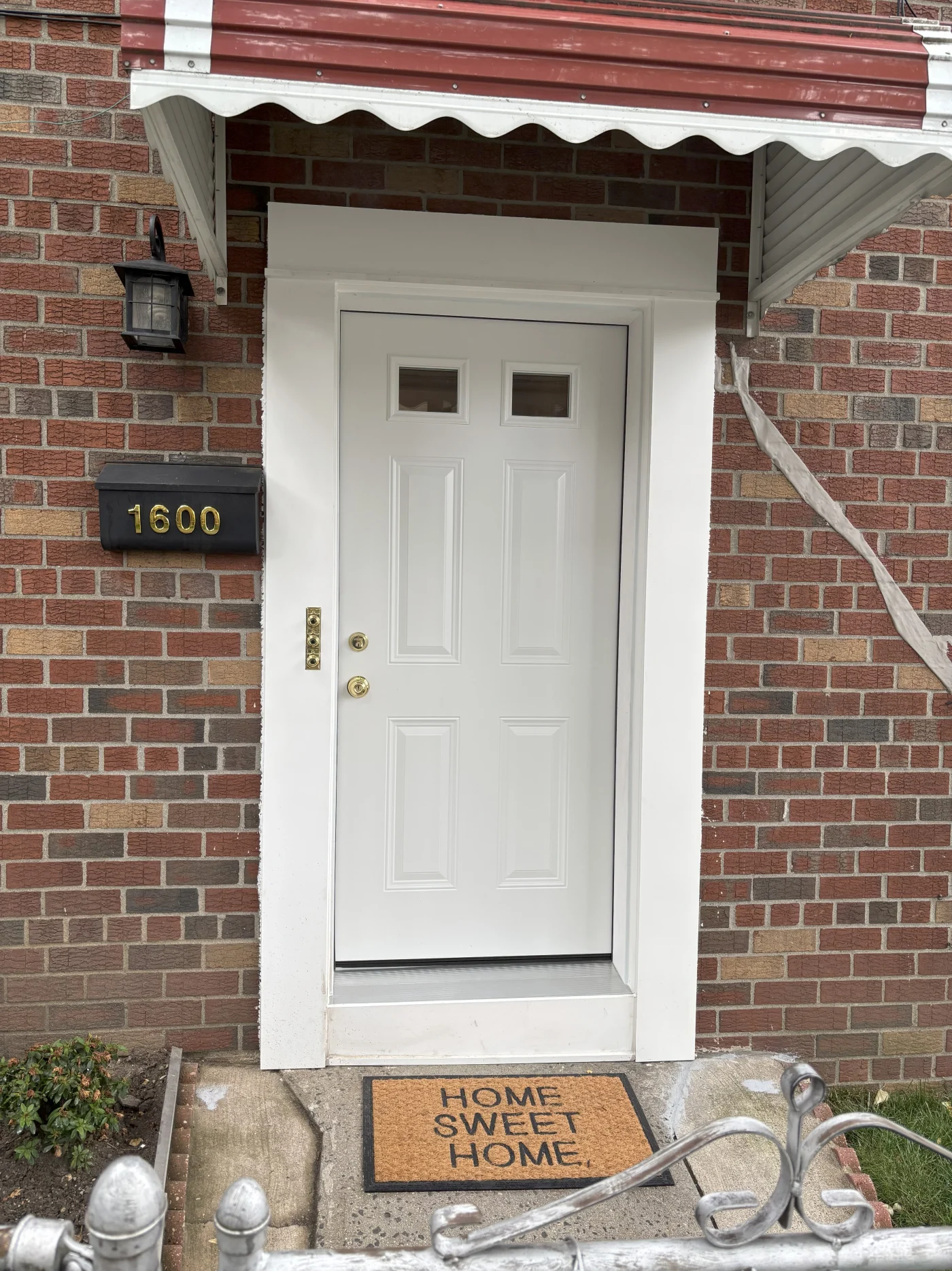 A modern black front door with four rectangular glass panels arranged vertically, flanked by narrow sidelights and topped with a transom window.