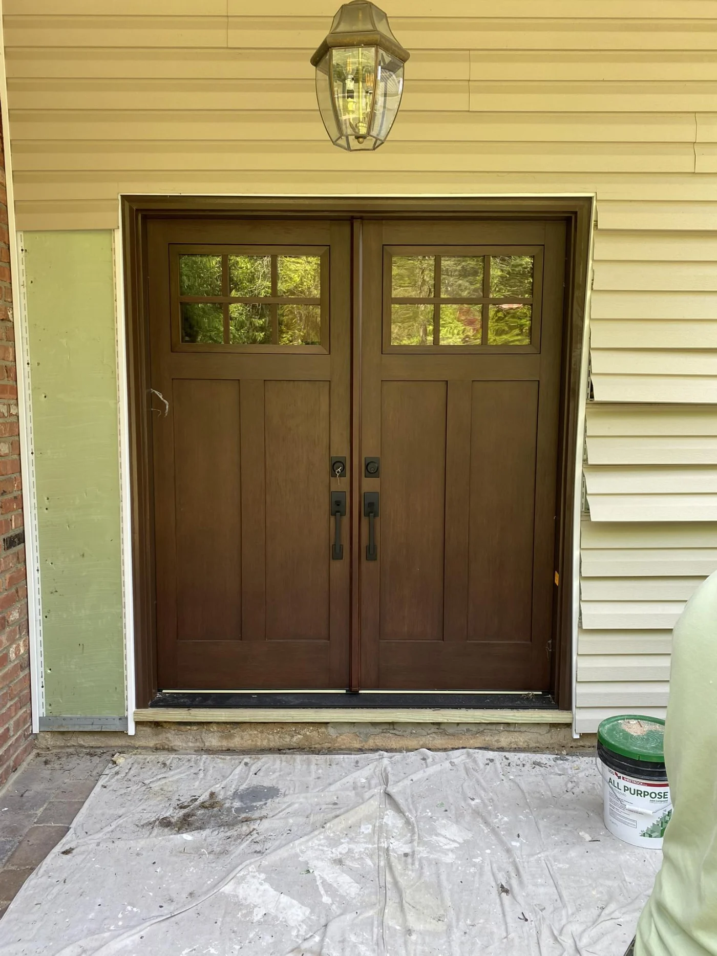 A dark-stained ProVia Signet fiberglass double entry door with Craftsman-style recessed panels, divided glass windows at the top, and matte black hardware, set against light-colored siding.