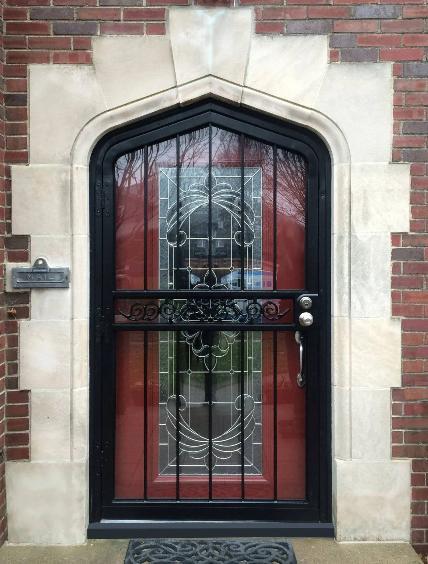 A custom Home Guard storm door with an arched top, decorative wrought iron grille, and ornate leaded glass over a deep red entry door.