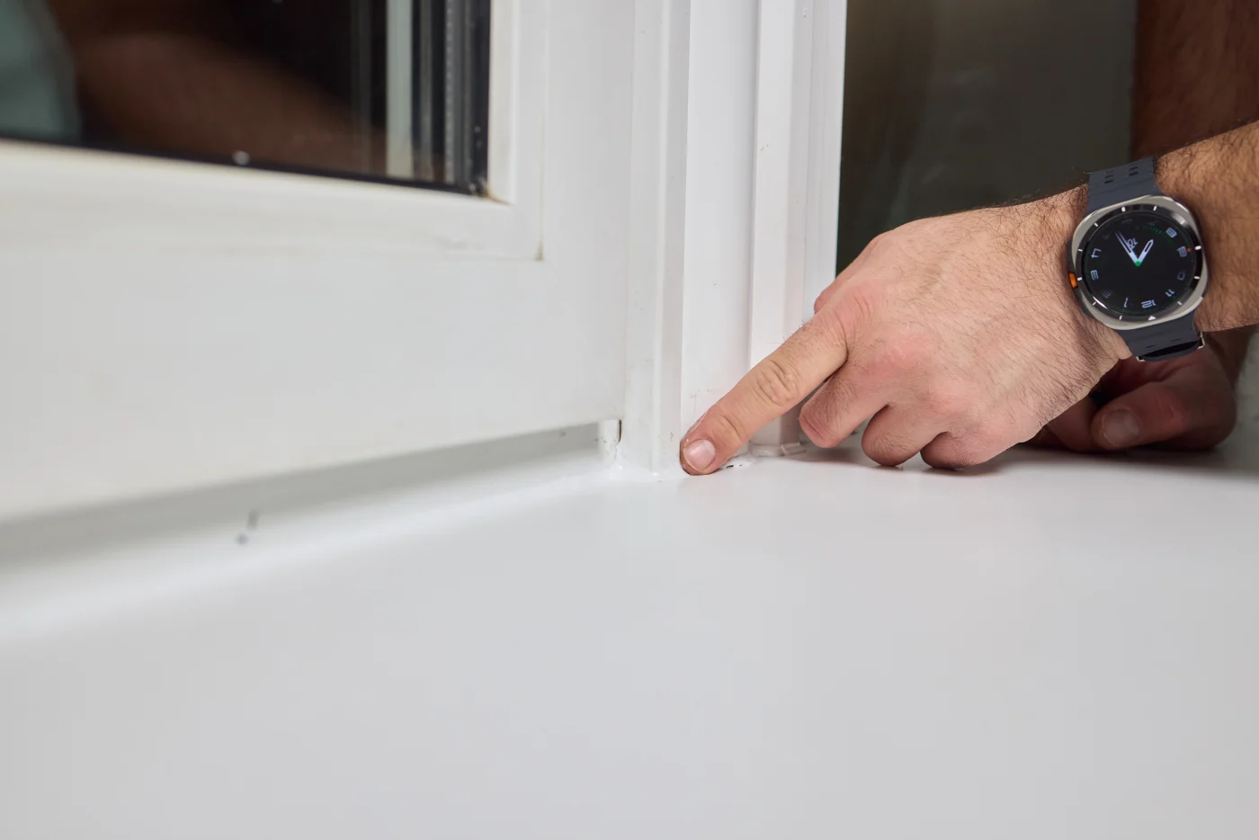 A close-up of an installer’s hand pointing to a precise bead of sealant in the corner of a freshly installed white window frame. The clean lines, spotless sill, and sharp detail reflect a level of care, quality, and finish that only comes from crews who hold every install to the golden standard.
