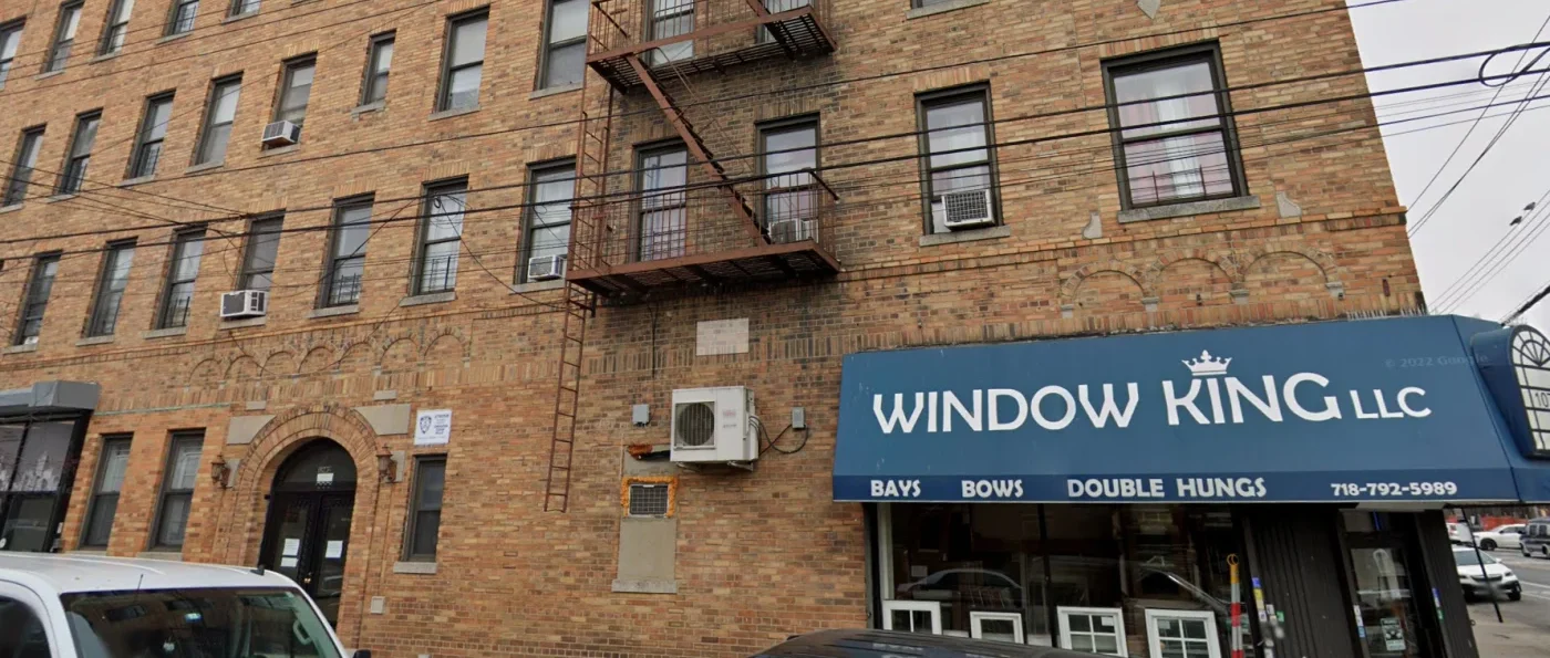 Street-level view of Window King’s brick-and-mortar location in the Bronx, housed in a classic multi-story brick building. The storefront features a bold blue awning with the Window King logo and contact information, along with neatly displayed window samples. The setting reflects the company’s deep neighborhood roots, humble beginnings, and proud presence in the heart of the community they’ve served for over 30 years.