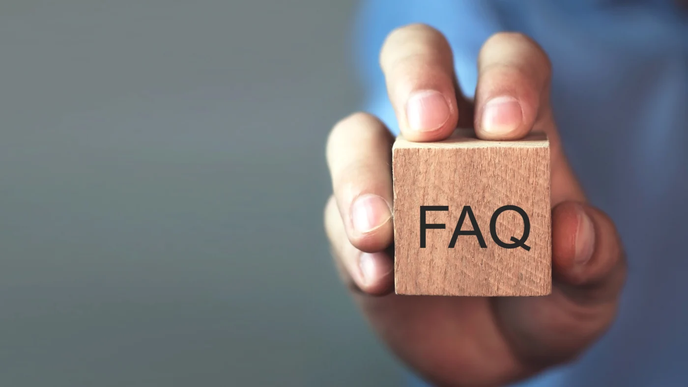 Window King | Company FAQs | Window & Entry Door Replacement | NY Metro Close-up of a hand holding a small wooden block with the letters “FAQ” printed on it. The background is blurred, drawing focus to the block.