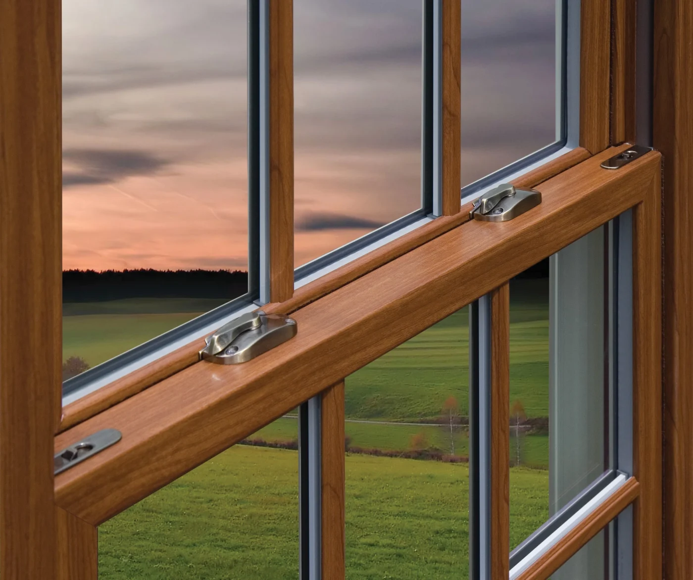 Window King – Loyal To OKNA Windows For 20+ Years Close-up of an OKNA 800 Series double-hung window with a warm woodgrain interior finish. The streamlined sash design and durable locks highlight traditional wood style without the upkeep, framing a sunset view over open green fields.