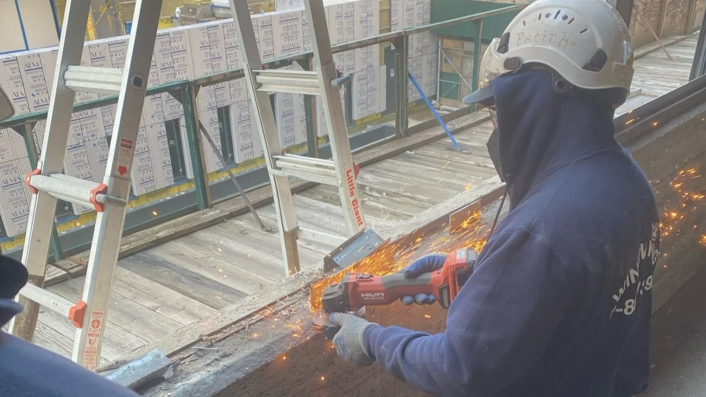 A Window King installer uses a power tool to prep a large opening, sparks flying as metal is cut with precision. Wearing safety gear and a Window King hoodie, the worker demonstrates the company’s commitment to careful preparation and workmanship that reflects pride in their family name.
