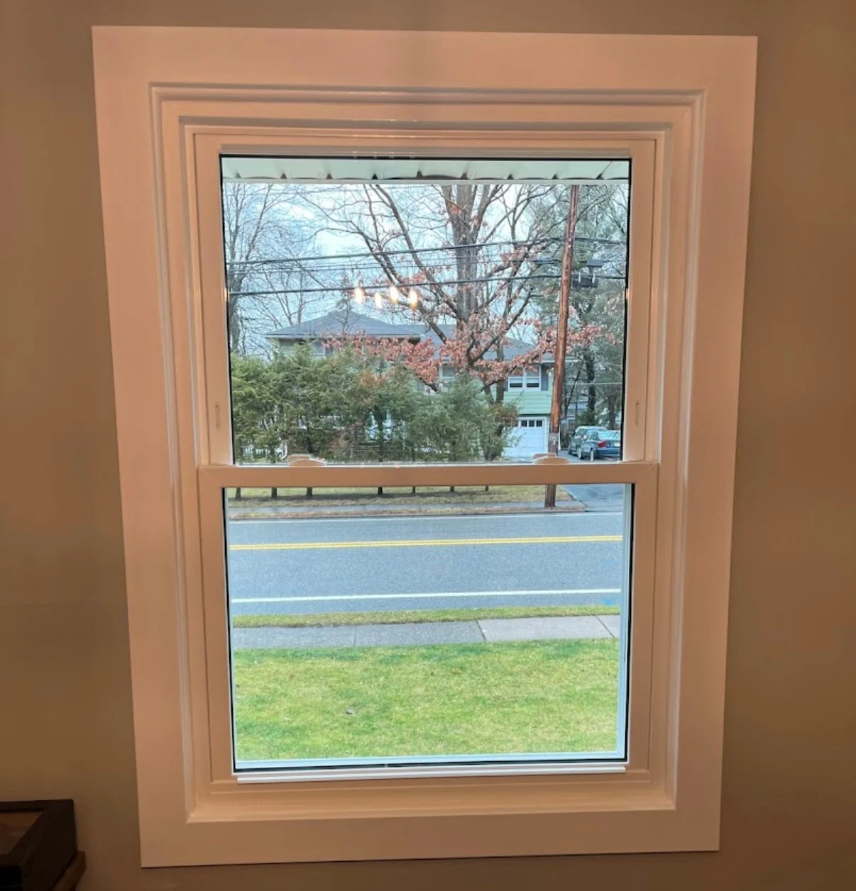 Interior view of a newly installed white double-hung replacement window in a Scarsdale, NY home, showing clean trim work and a clear view of the street.