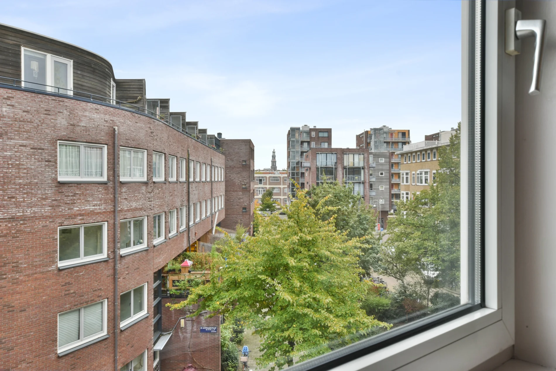 View from inside a newly installed residential window overlooking a cityscape with brick apartment buildings, trees, and natural daylight.