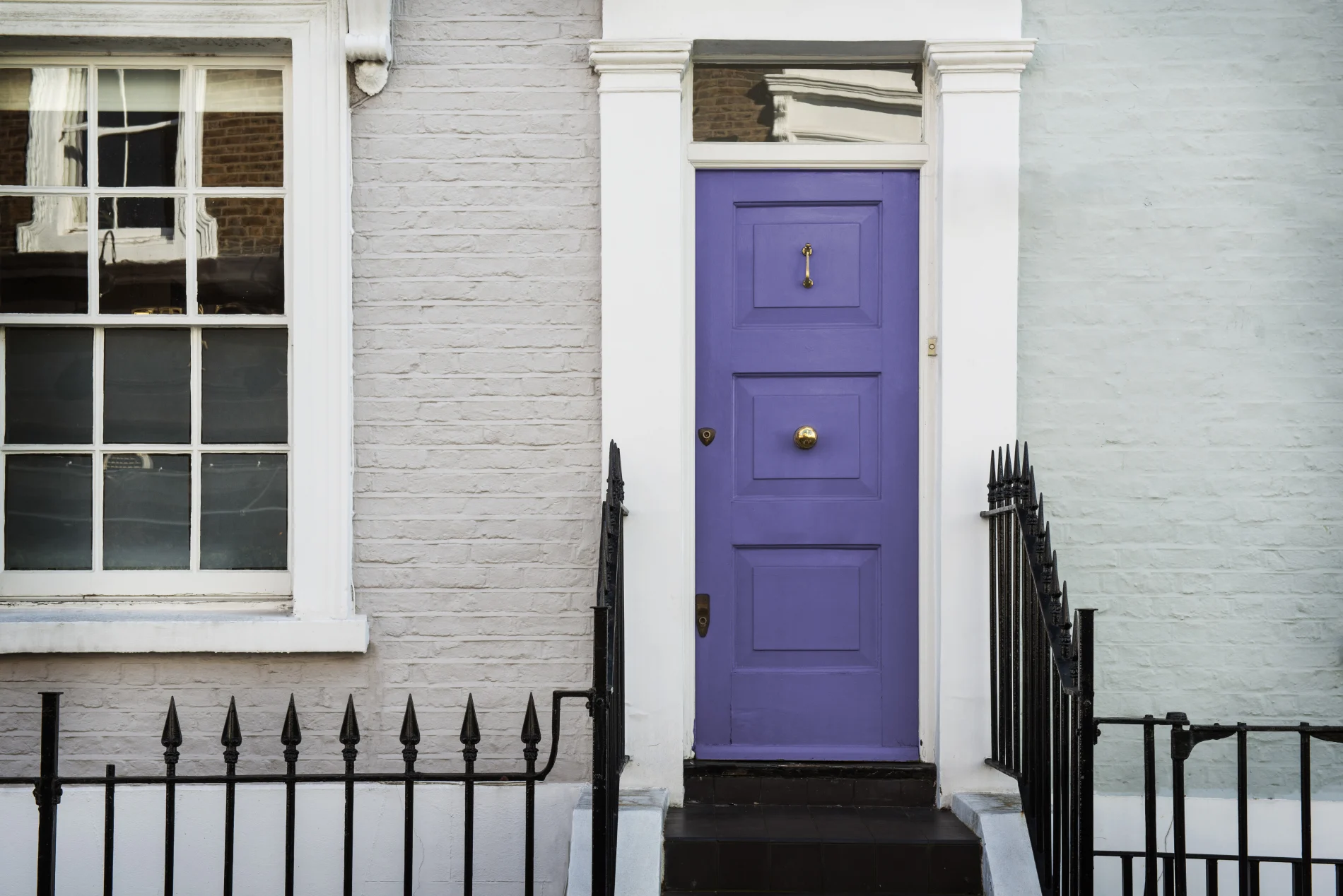 Elegant townhouse entry with a bold purple front door, white-painted brick façade, brass hardware, and black wrought iron railings.