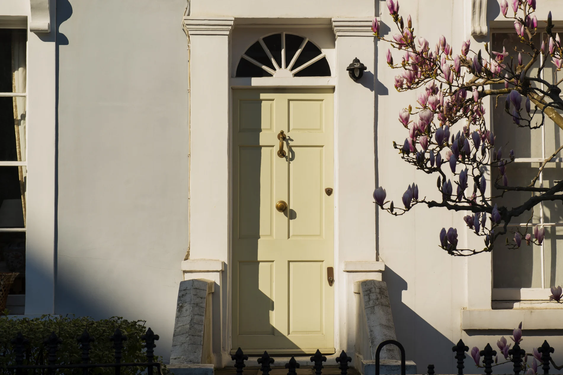 Stylish Bronx townhouse entry with front door, decorative wreath, brick façade, wrought iron gate, tree shadows, and warm natural sunlight.