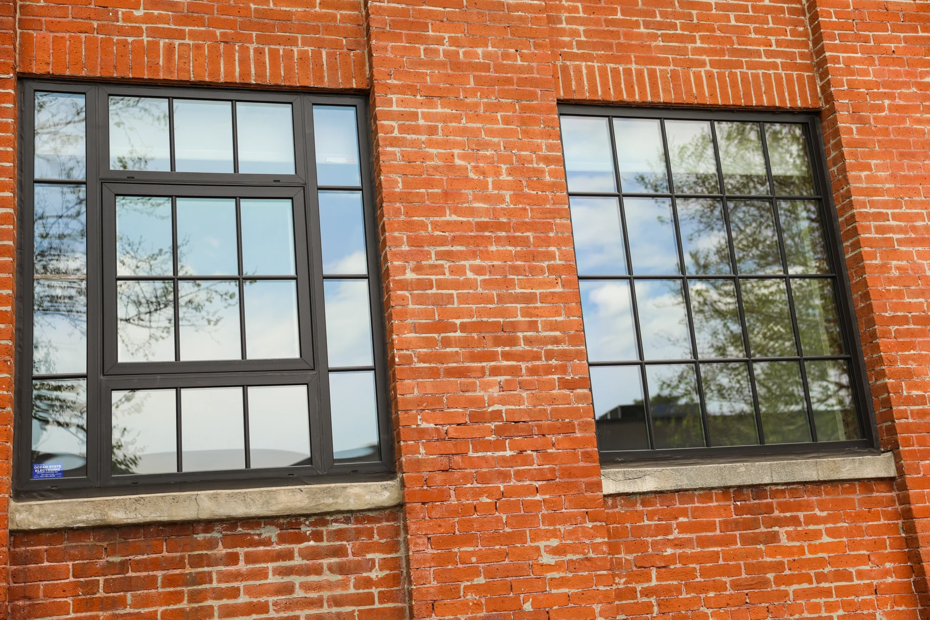 Modern black-framed replacement windows installed in a red brick building, reflecting trees and sky with clean industrial-style design.